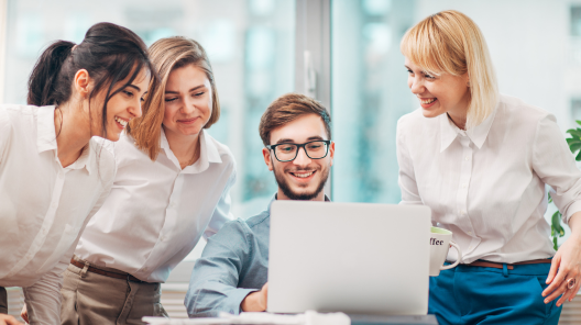 Grupa stojących kobiet dookoła mężczyzny siedzącego przy laptopie - wszyscy wpatrzeni w komputer